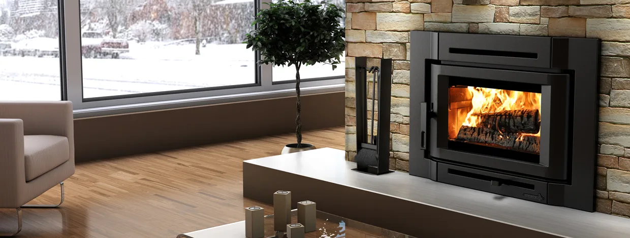 An Enerzone wood insert burning in a stacked-stone fireplace beside a window onto snow