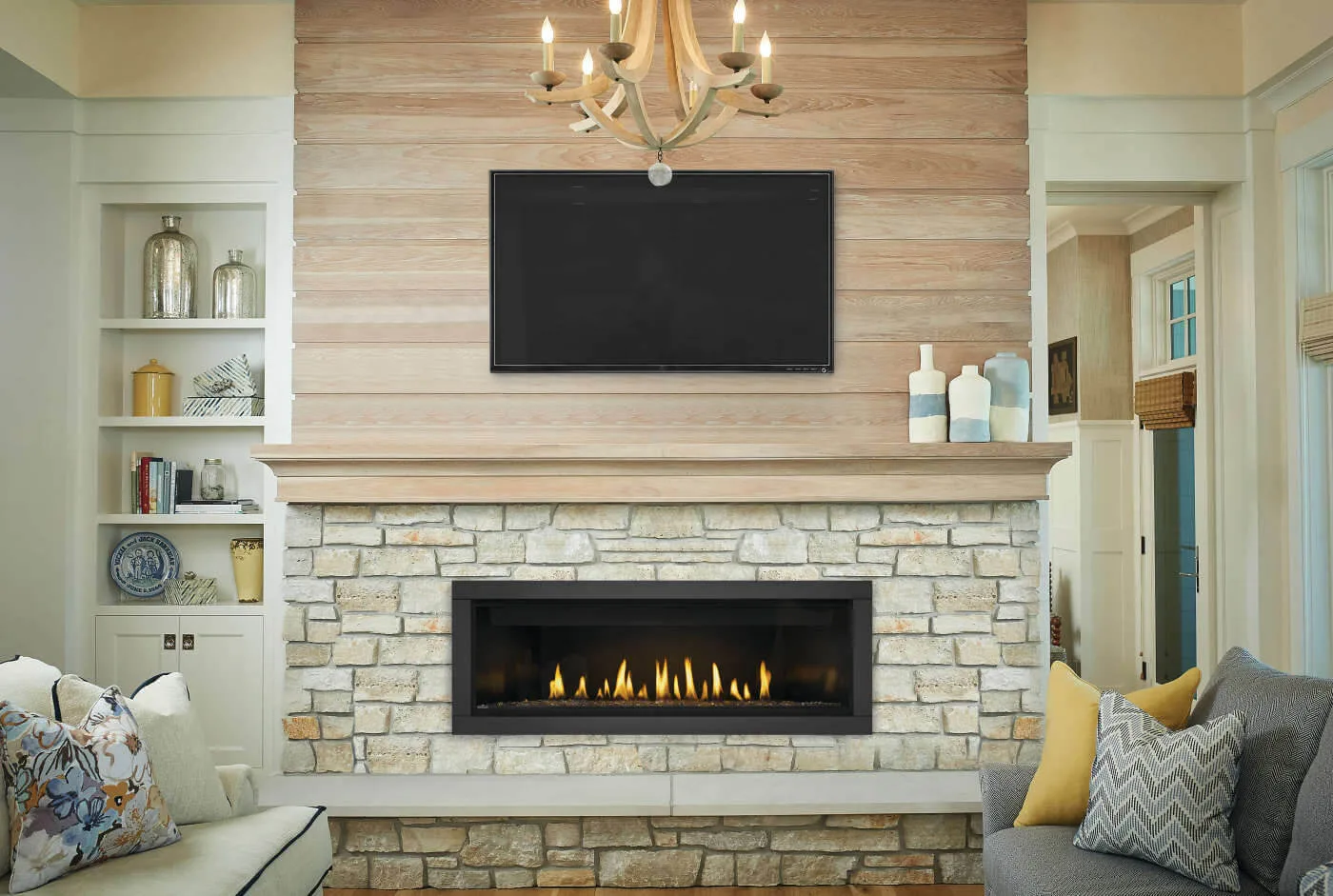 A Napoleon Ascent Linear gas fireplace lit in a pale stone breast below a wall-mounted TV