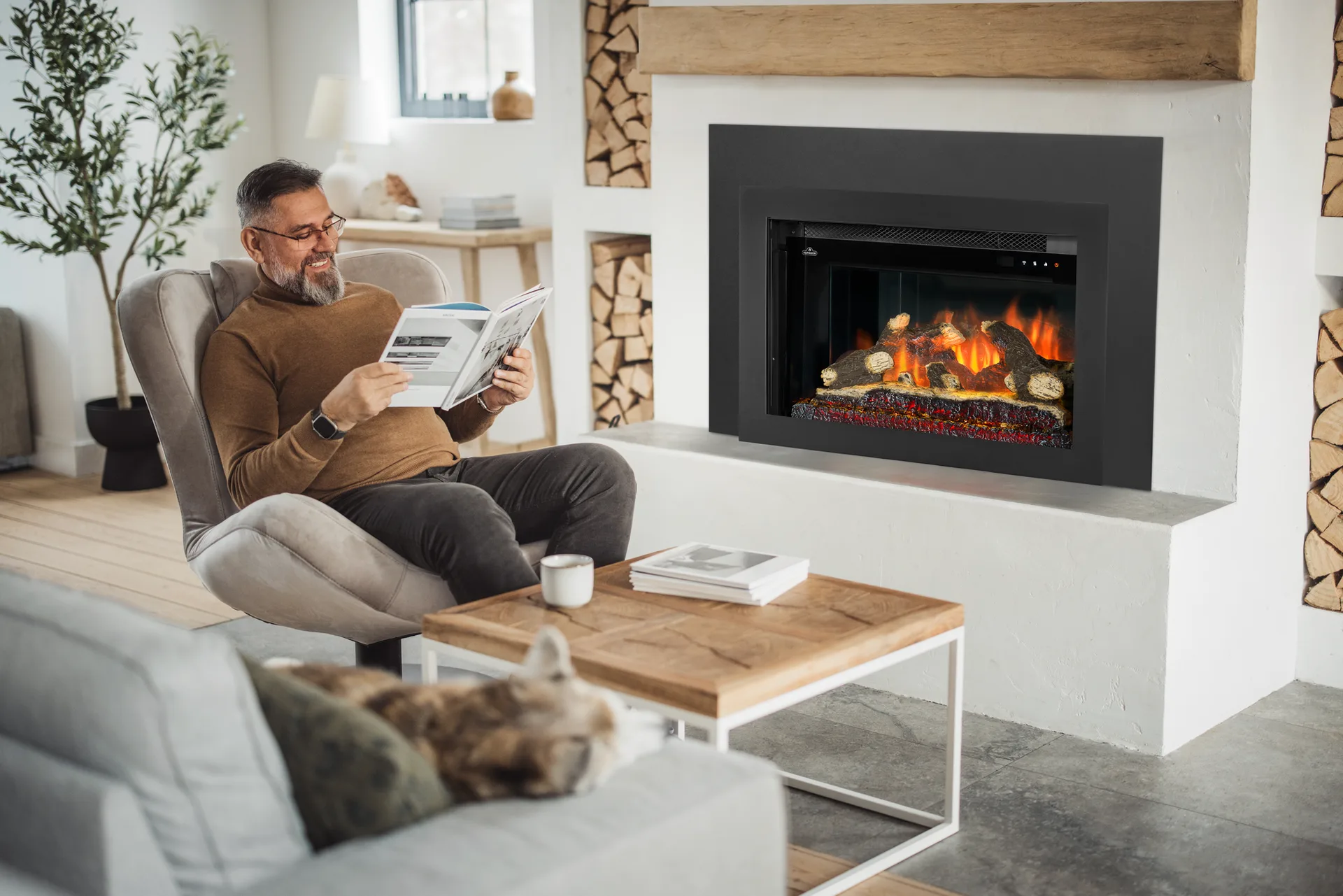 Man reading in a chair beside an electric insert in a white plaster fireplace