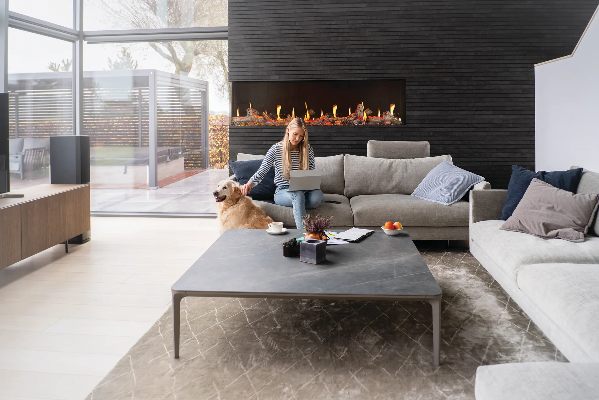 Woman and her dog beside a long linear fireplace set into a dark brick wall
