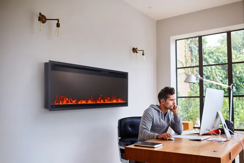 A man working at his desk beside a wall-mounted linear electric fireplace