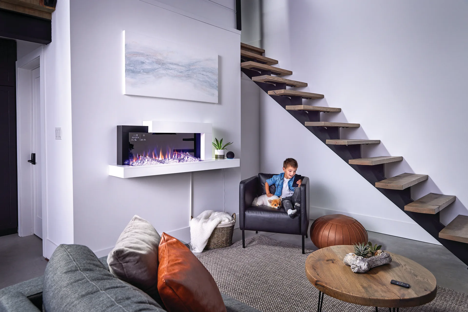 Child in a chair beside a wall-mounted electric fireplace under a timber staircase