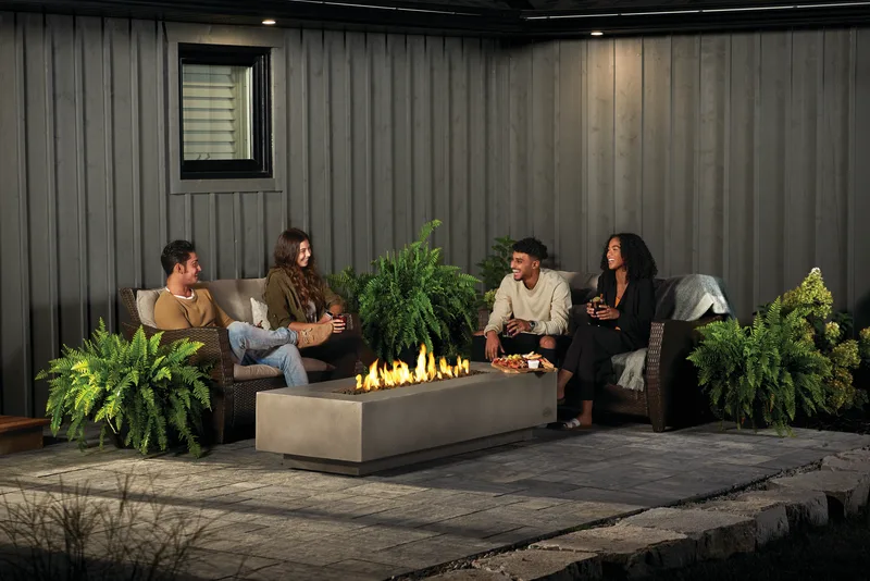 Four friends on outdoor sofas around a long lit fire feature