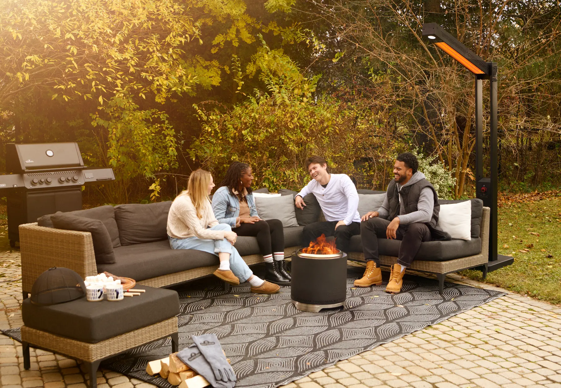 Four friends around a smokeless fire pit on a paver patio in autumn