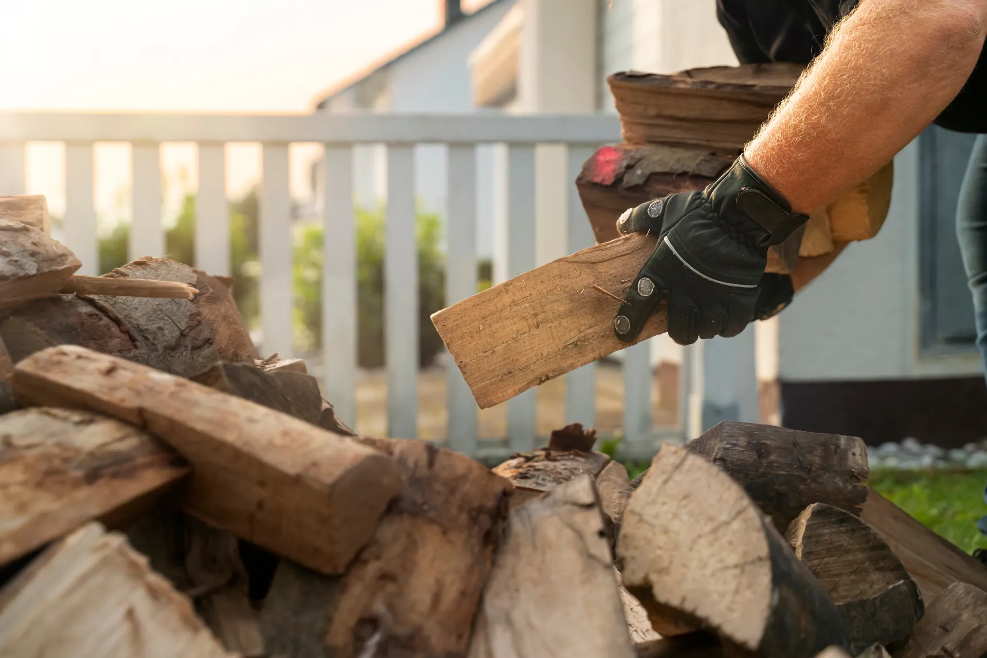 Gloved hands carrying split firewood on a deck