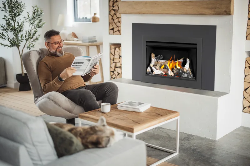 A man reading the paper beside a lit gas insert flanked by firewood niches