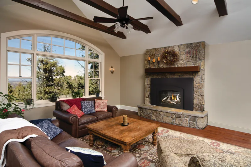 A gas insert in a stone fireplace under a beamed vaulted ceiling