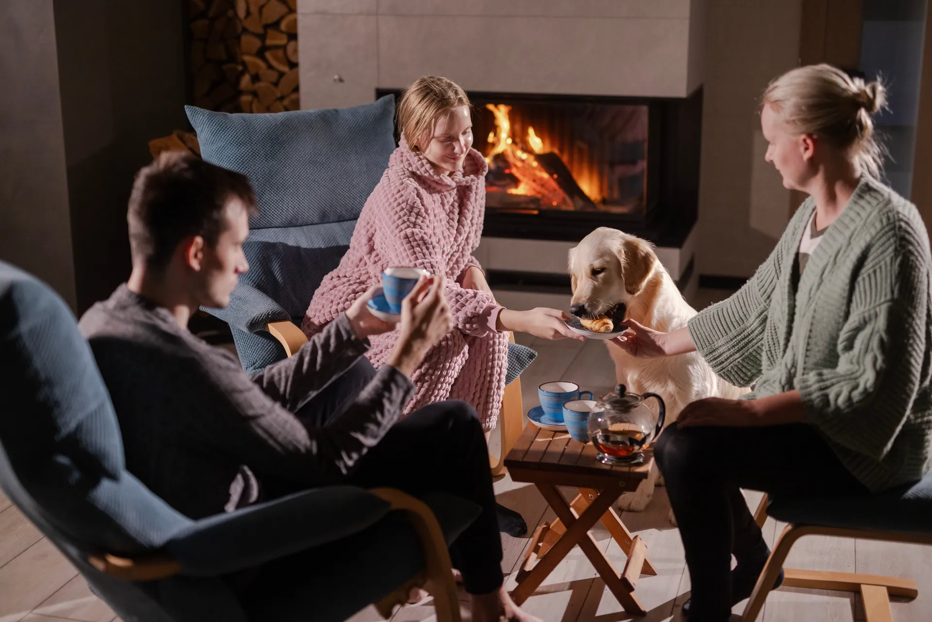 Family and a dog by an outdoor fireplace, wrapped in blankets