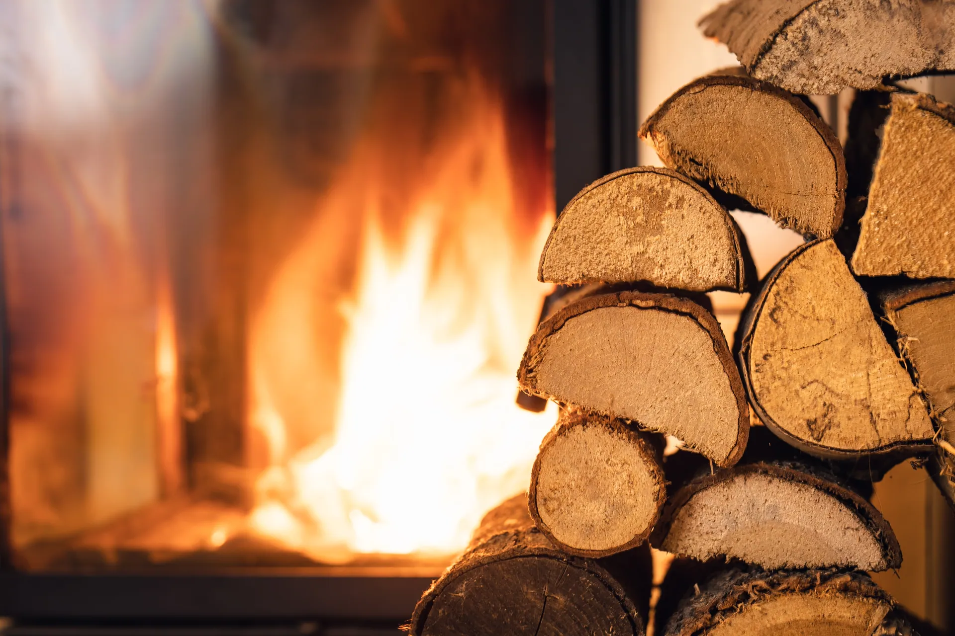 Fire burning behind glass beside a stacked woodpile