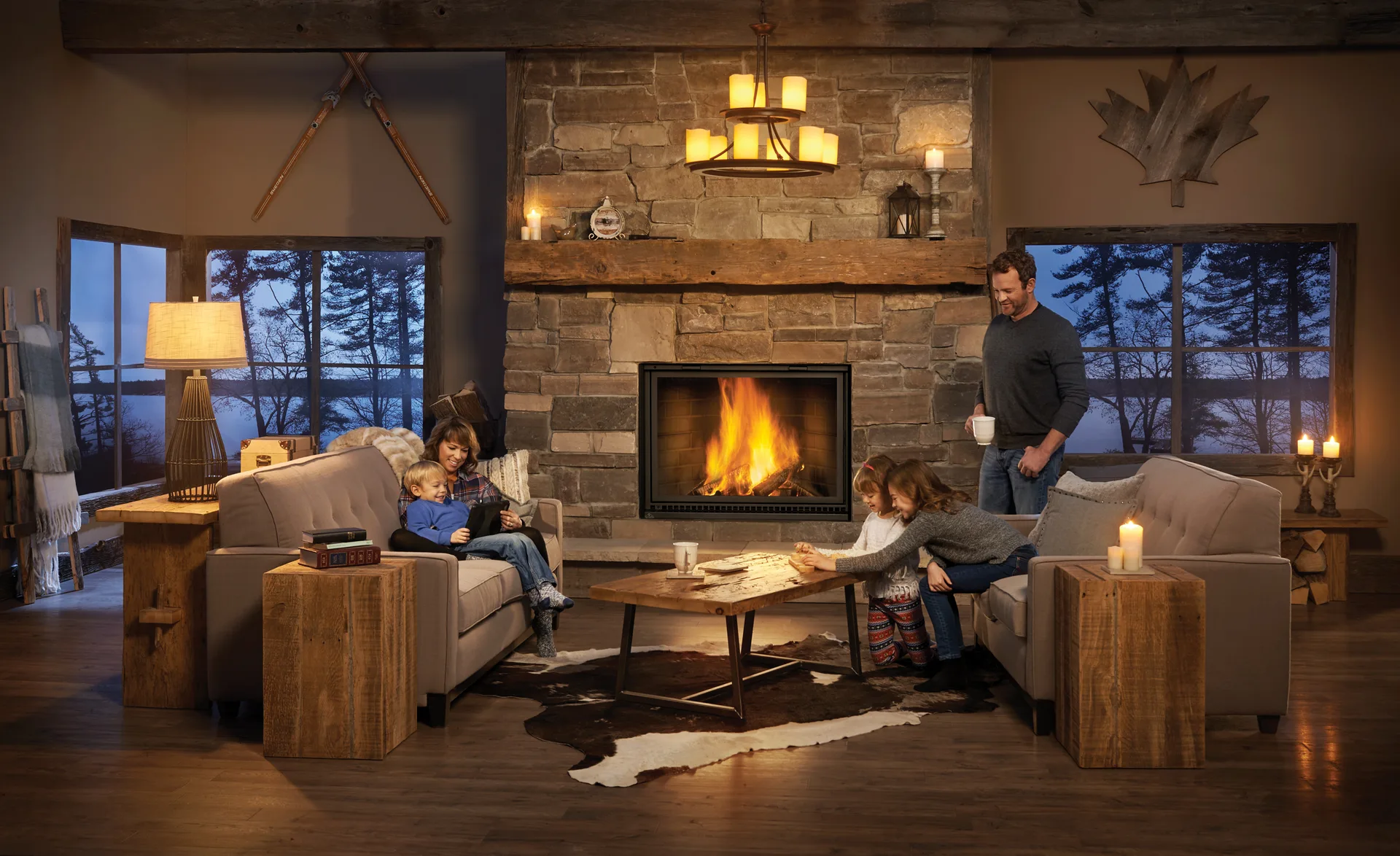 A family of five around a lit wood fireplace in a stone chimney breast at dusk