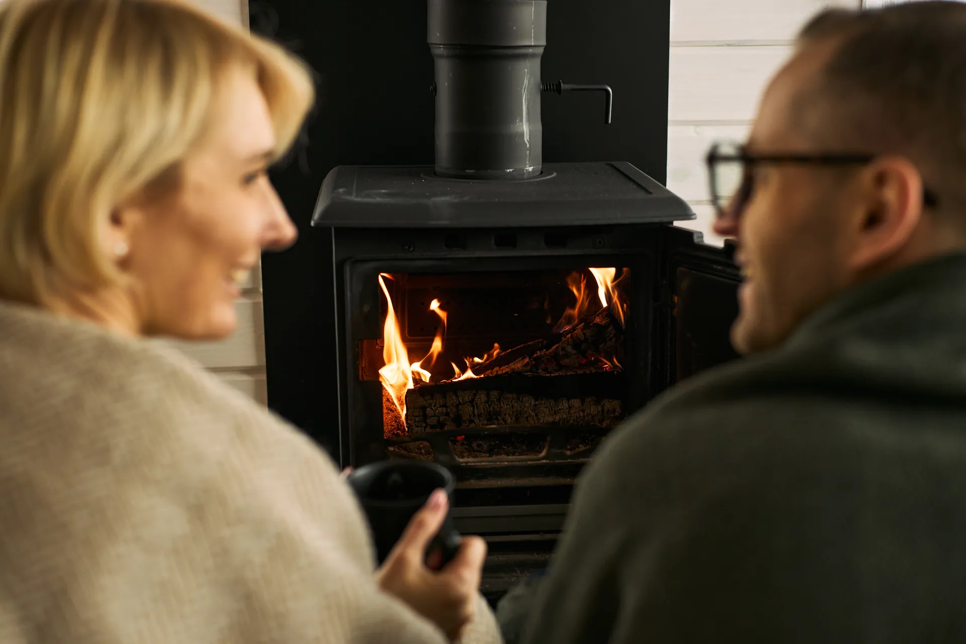 Couple with mugs beside a freestanding wood stove